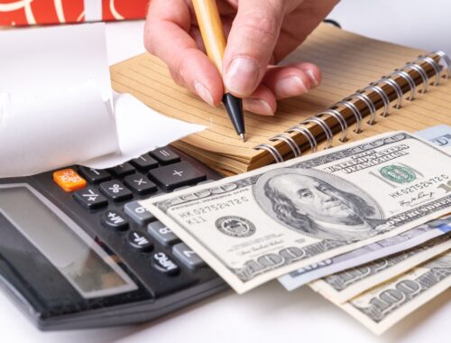 A woman's hand writing down the cash flow in a notebook with a pen, counting cash on a calculator
