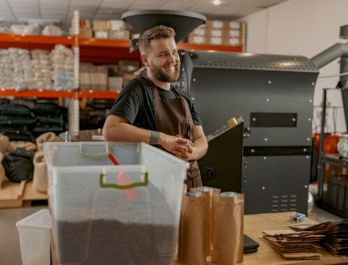 Portrait of smiling business owner on background of own small coffee factory looking away
